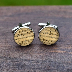 Elegant silver musical note cufflinks with vintage sheet music on dark wood background