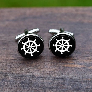Close-up of nautical steering wheel cufflinks on a vintage wooden surface