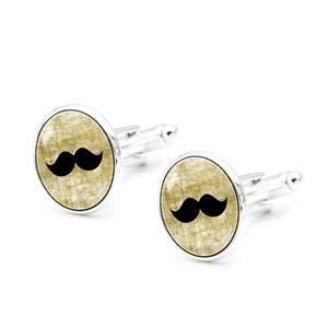 Macro view of silver cufflinks featuring a black mustache pattern on golden fabric texture