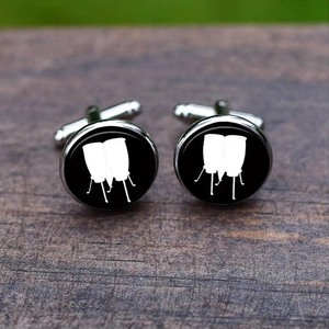 Close-up of silver-tone cufflinks featuring white conga drum silhouettes on wood surface