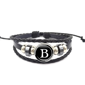 Dettaglio di un bracciale multistrato in pelle nera con ciondolo lettera B e corde intrecciate
