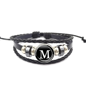 Dettaglio del bracciale multistrato in pelle intrecciata con ciondolo in vetro lettera M