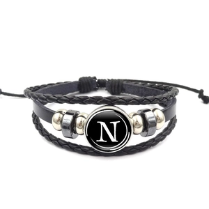 Dettaglio del bracciale multistrato in pelle nera con ciondolo a lettera N bianca