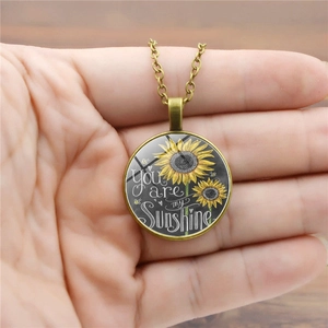 Detalle del collar con colgante de girasol y texto You are my sunshine en marco bronce