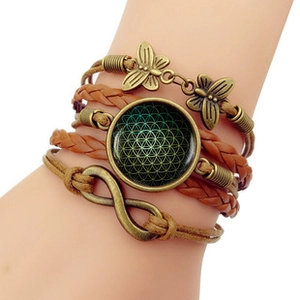 Détail d'un bracelet multicouche en cuir avec cabochon fleur de vie et pendentif papillon