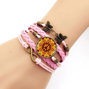 Détail du bracelet multicouche en cuir rose avec papillon en bronze et breloque tournesol