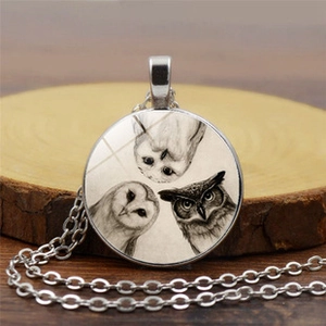 Detail view of round glass cabochon pendant with three artistic owl sketches in silver frame
