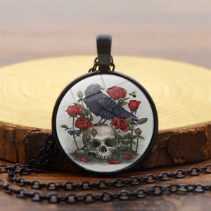 Close-up of gothic crow on skull and red roses artwork inside black glass pendant