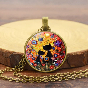 Artistic pendant necklace detail with two black cats on a glass gem and bronze chain