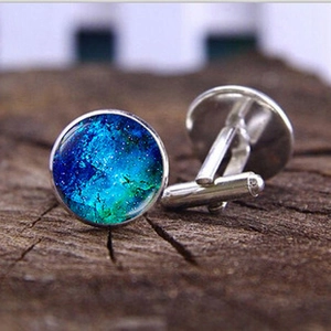 Macro shot of silver cufflinks with blue nebula glass dome on natural wood background