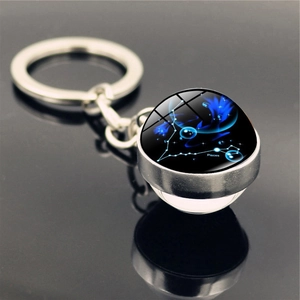 Detailed close-up of Pisces constellation glass ball keychain with blue nebula background