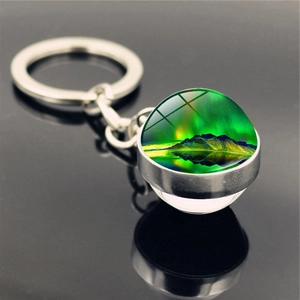 Macro shot of double-sided glass orb keychain featuring aurora borealis and snow mountains