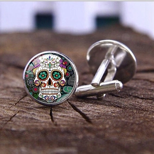 Detalle de gemelos plateados con coloridos patrones de calaveras mexicanas sobre fondo de madera