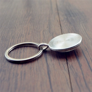 Silver metal keychain base with oval charm holder and non-slip texture on wood background