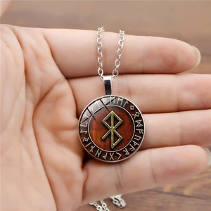 Macro detail of vintage Viking rune pendant with gold symbols and silver chain held in hand