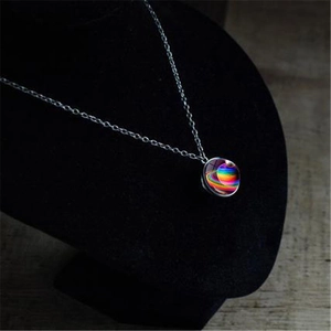 Macro detail of round galaxy planet pendant with colorful Saturn ring on black velvet