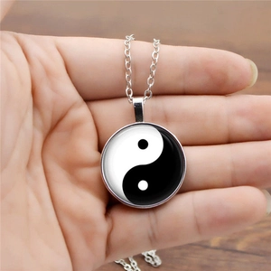 Detailed close-up of Yin Yang glass dome pendant held in hand with silver chain necklace
