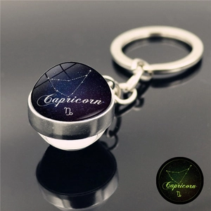 Detail view of Capricorn zodiac glass orb keychain with glowing effect on reflective surface