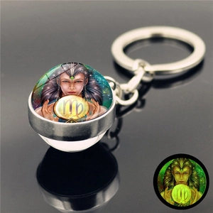 Glow-in-the-dark Virgo zodiac glass ball keychain with silver metal ring on dark background