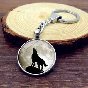 Detailed view of the luminous howling wolf glass dome keychain on a rustic wood background