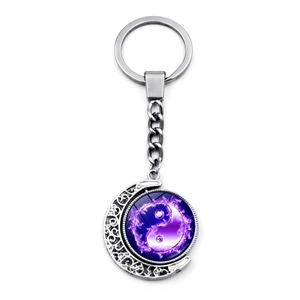 Macro detail of rotating yin yang pendant on a silver moon keychain with purple floral accents