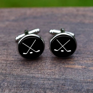 Close-up of hockey theme cufflinks with crossed sticks on textured wooden surface