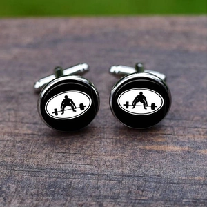 Macro detail of silver weightlifting cufflinks featuring a black athlete silhouette on wood