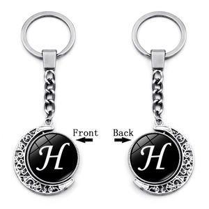 Detail of a rotating silver crescent moon keychain with double-sided letter H design