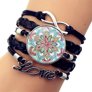 Macro detail of multilayer leather bracelet featuring Love charm and mandala glass dome