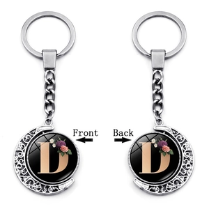 Detail of a rotating silver moon keychain with floral letter D on both sides
