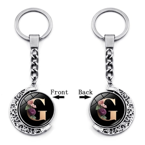Close-up of double-sided rotating moon keychain featuring floral letter G pendant