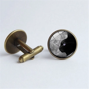 Close-up of bronze cufflinks featuring black cat pattern under glass dome on gray background