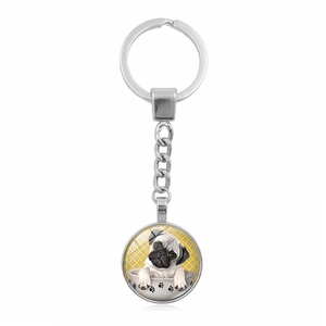 Close-up of a silver keychain with a round pug dog illustration under glass dome pendant