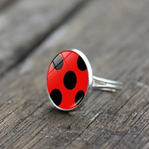 Adjustable silver ring with red polka dot glass oval pendant on a dark wood background
