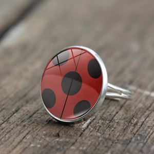 Close-up of adjustable silver ladybug pattern ring on a rustic wooden background