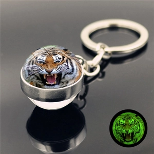 Close-up of luminous tiger head glass ball keychain with green glowing effect in dark