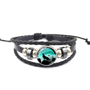 Detail eines Lederarmbands mit Glasanhänger-Motiv eines heulenden Wolfes im Mondlicht