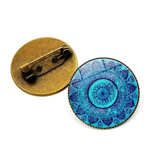 Detalle frontal y posterior de un broche de mandala en bronce con cristal azul