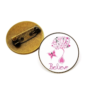 Détail de la broche en verre avec ruban rose et texte Believe sur base en bronze