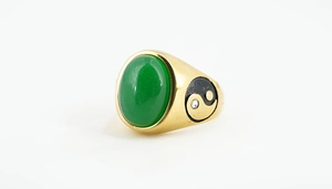 Macro detail of gold ring with green oval gemstone and yin yang relief pattern