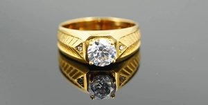 Macro detail of men gold ring with prong-set zircon and arrow-patterned thick band