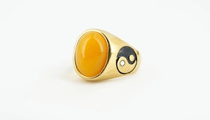 Detailed close-up of men's gold ring with oval yellow gemstone and Tai Chi symbol engraving