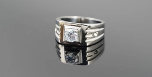 Macro shot of silver men's ring with a central round zircon on reflective surface