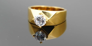 Macro shot of gold titanium ring with round brilliant cut zircon on reflective background