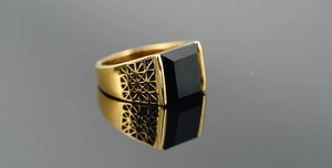 Macro detail of men's gold ring showing square black stone and geometric side cutouts