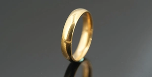 Polished golden stainless steel ring reflecting on a dark grey mirror surface