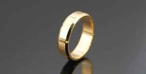 Macro shot of minimalist gold ring with polished finish and beveled edges on dark base