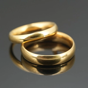 Polished gold titanium steel minimalist rings for couples on reflective dark surface