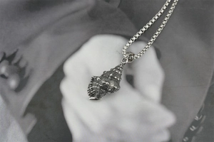 Gros plan détaillé d'un pendentif conque vintage en acier sur une chaîne à mailles box