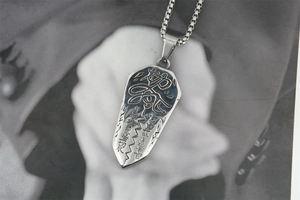 Macro shot of silver titanium steel shield pendant with artistic Chinese calligraphy engraving